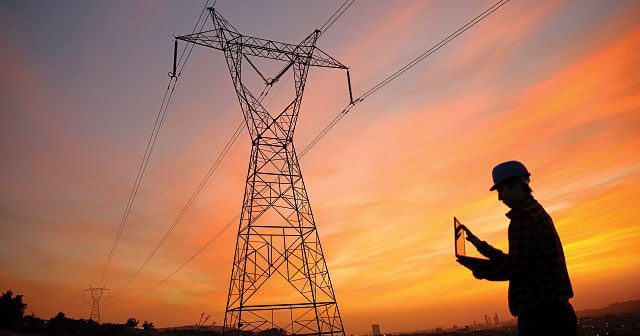 engineer at sunset on laptop with powerline