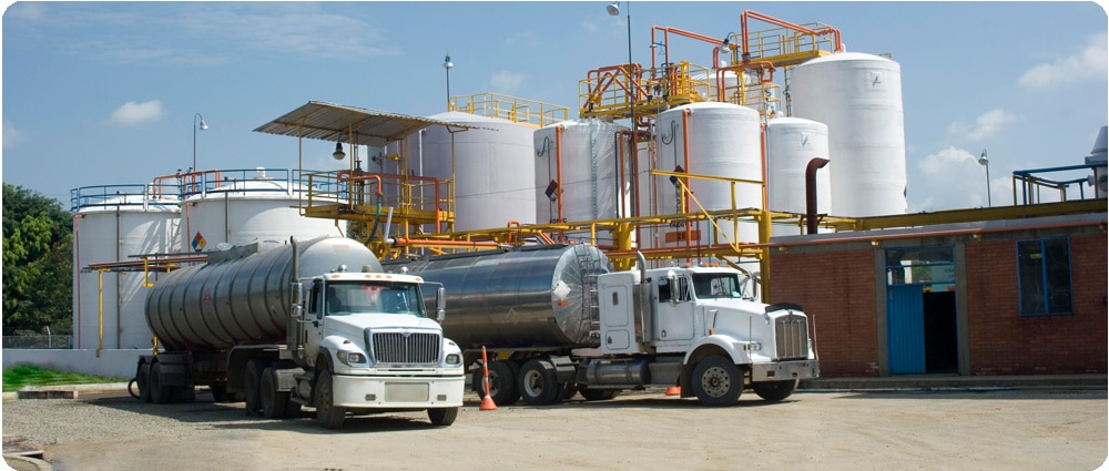 Two fuel trucks in front of storage tanks