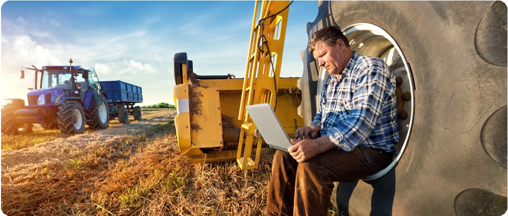 Farmer on laptop next to tractor