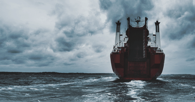 A red ship out sailing on the ocean as overcast covers the sky and dark waters