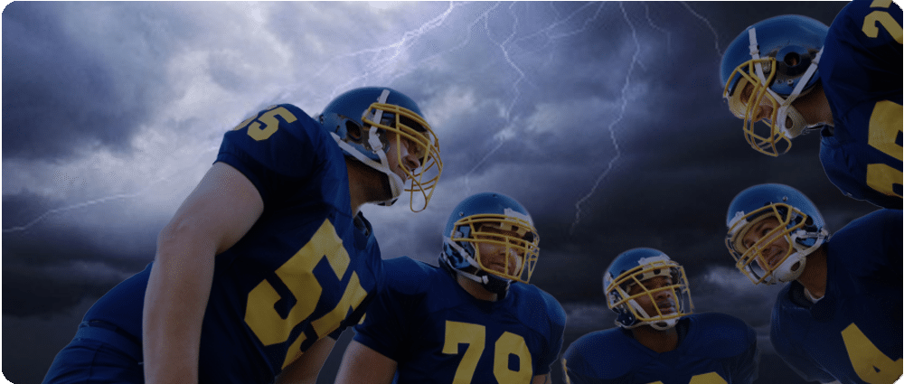 Football players huddle with lightning in the sky