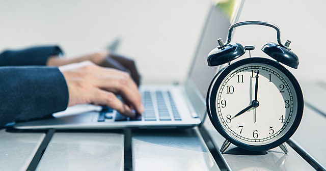 Hands on laptop near alarm clock